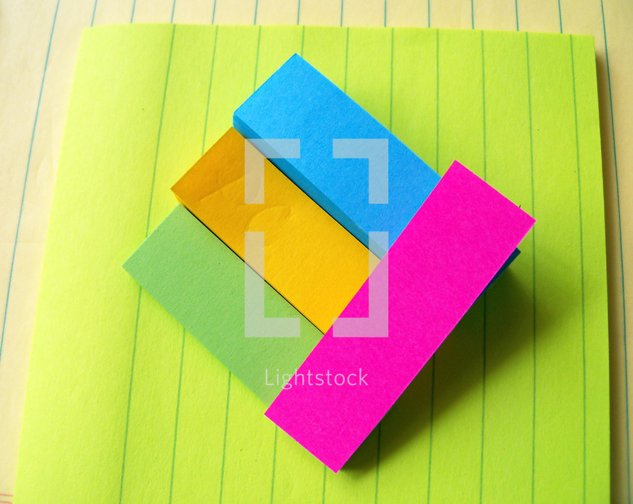 Various colors and types of paper with layers of colored sticky note paper raised above the surface to create a 3D effect with various colored sticky notes and paper.  