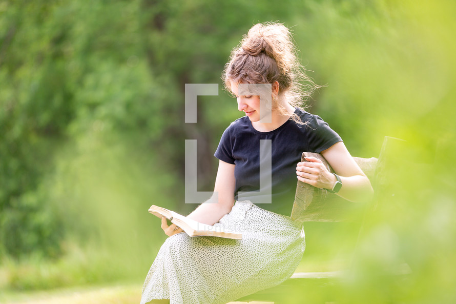 Woman smiling and reading Bible outdoors on bench
