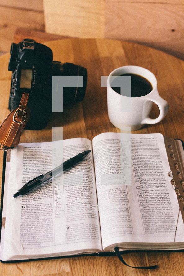 An open Bible, cup of coffee, and a camera on a table.