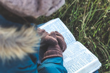 a woman in a coat and gloves praying over a Bible 