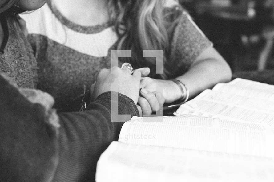 Two women clasp hands as they study the Bible.