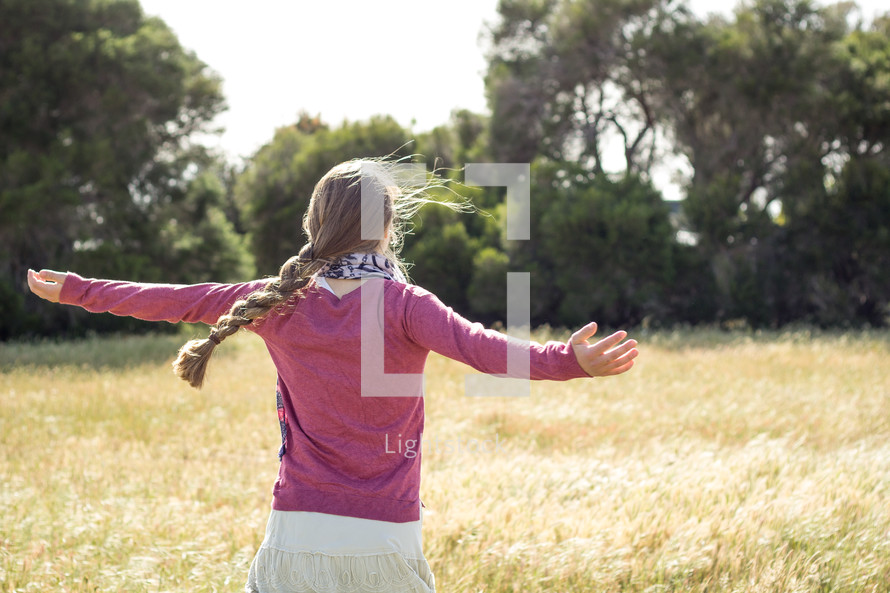 teen girl with braided hair standing in a field with outstretched arms 