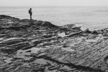 a woman with a backpack standing on a rocky shore 