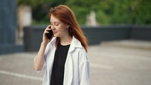 Red-haired girl walks down the street and talks on the phone.