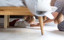 mother pulling young daughter out from under the bed 