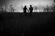 silhouette of a couple holding hands in a field