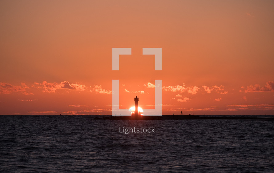 sun setting behind a lighthouse 