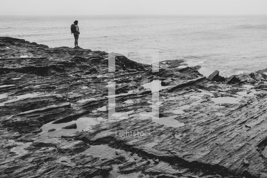 a woman with a backpack standing on a rocky shore 