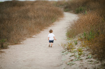 toddler standing on a sandy path 