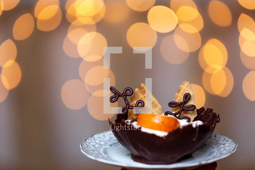 Chocolate bowl with orange mousse and chocolate accents with lights in background