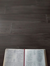 An open Bible on a dark wood table with space for text.