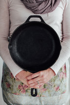 a woman holding up a cast iron skillet 