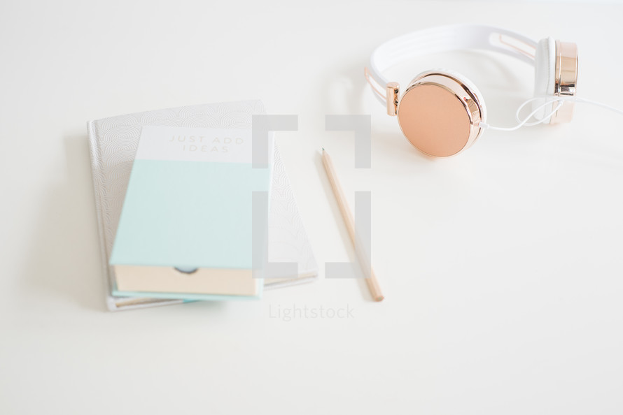 pencil, book, journal and headphones on a white desk 