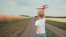 Future Pilot. Child boy runs with toy airplane on wheat field. Boy dreams of flying. Carefree boy playing outdoors. Happy kid running in nature, playing with toy airplane. Concept of child kindness.