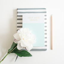 pencil, book, journal and flowers on a white desk 