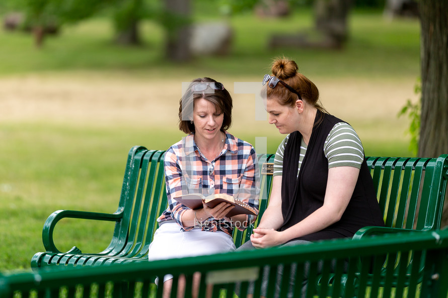 Two women studying the Bible on a park bench