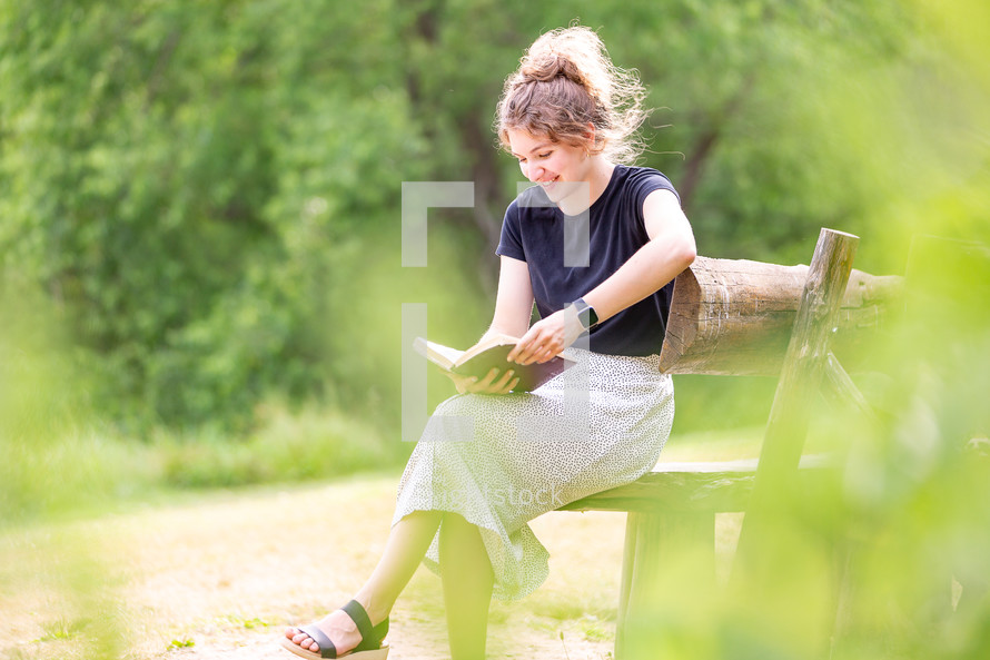 Woman smiling as she reads the Bible on a bench