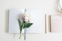 flowers on a journal, notepad, and pencil on a desk 