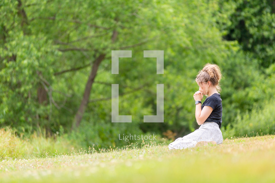 Young woman praying in a grassy field