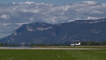 Small propeller aircraft on the ground with mountain range in the background under a cloudy sky