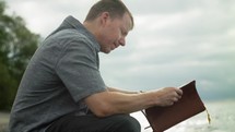 a man sitting on a beach reading a Bible and praying 