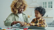 Little African American Boy Watching Photo Book and Talking with Mother at Home
