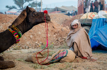 a man sitting next to a camel in India 
