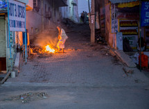 a man standing near a fire on the streets of India for warmth 