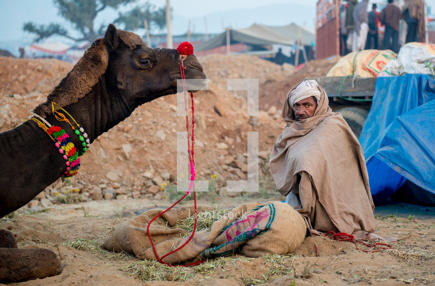 a man sitting next to a camel in India 