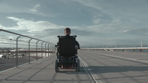 Wide shot of handicapped boy in electric wheelchair riding along the sea and enjoying fresh air
