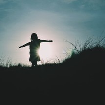 silhouette of a girl with outstretched arms at sunset 
