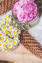 daisies, bowl of pink flowers, and pine cone on wood table 