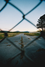 view of an old road through a chain link fence 