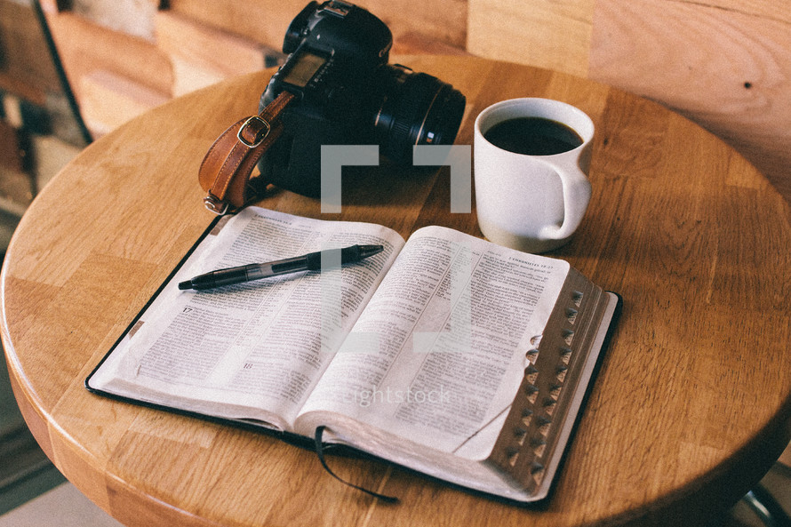An open Bible, cup of coffee, and camera on a table.