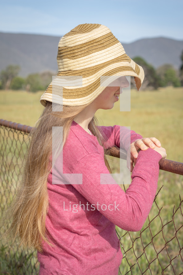 a girl in a straw hat looking over a fence 