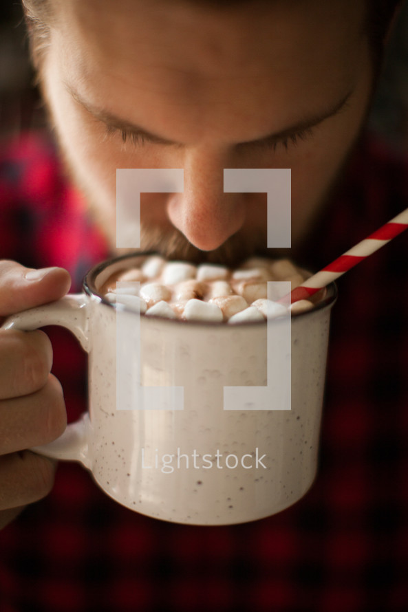a man in a plaid shirt drinking a mug of hot chocolate 