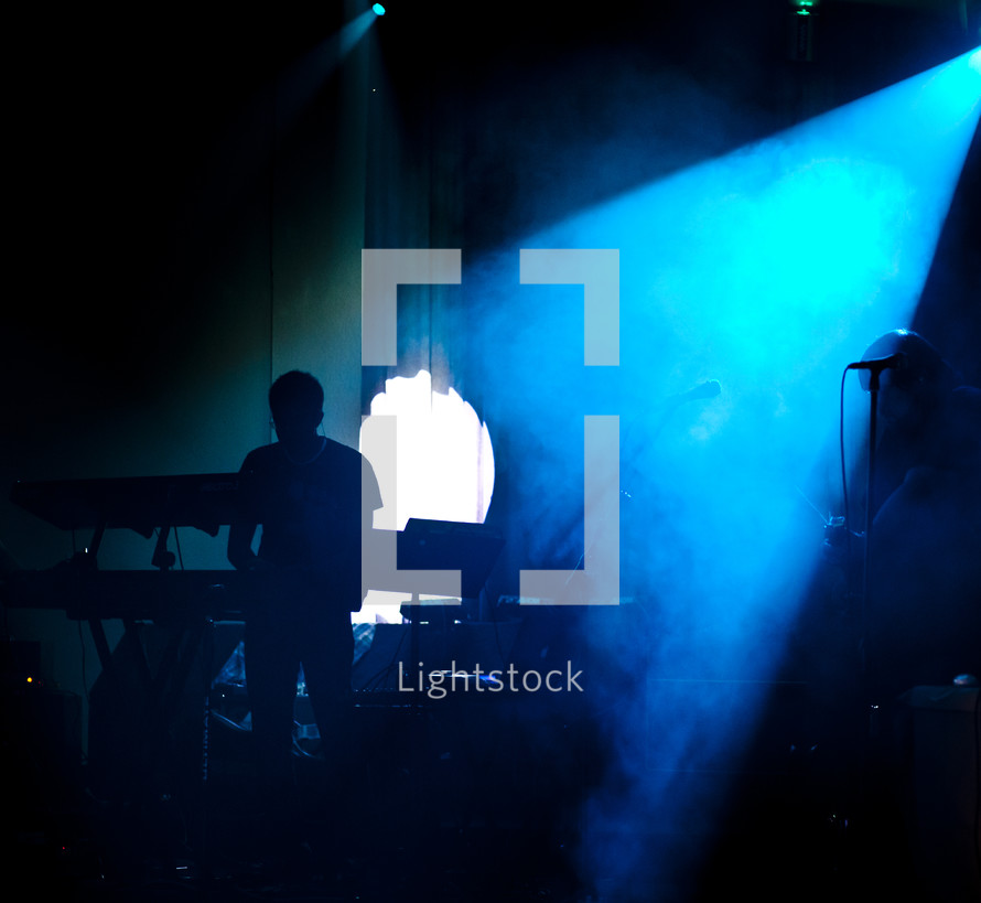 man on stage standing under a blue spot light