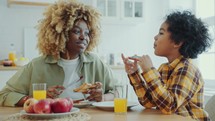 Happy African American Mother and Little Son Having Breakfast in the Kitchen
