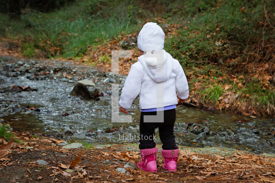a toddler girl standing by a creek 