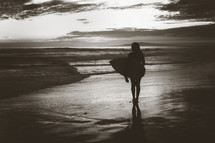 a silhouette of a female surfer standing on a beach 