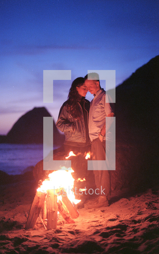 couple standing by a camp fire on a beach 
