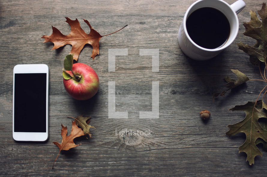 coffee cup, fall leaves, and apple on wood background 