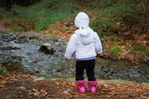 a toddler girl standing by a creek 