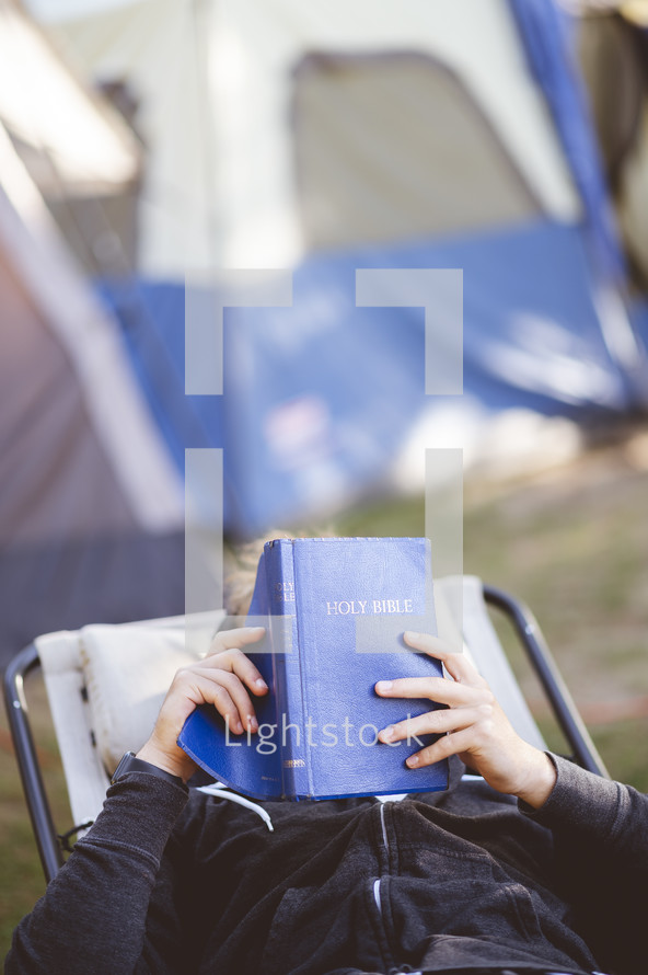 a man camping sitting outdoors reading a Bible 
