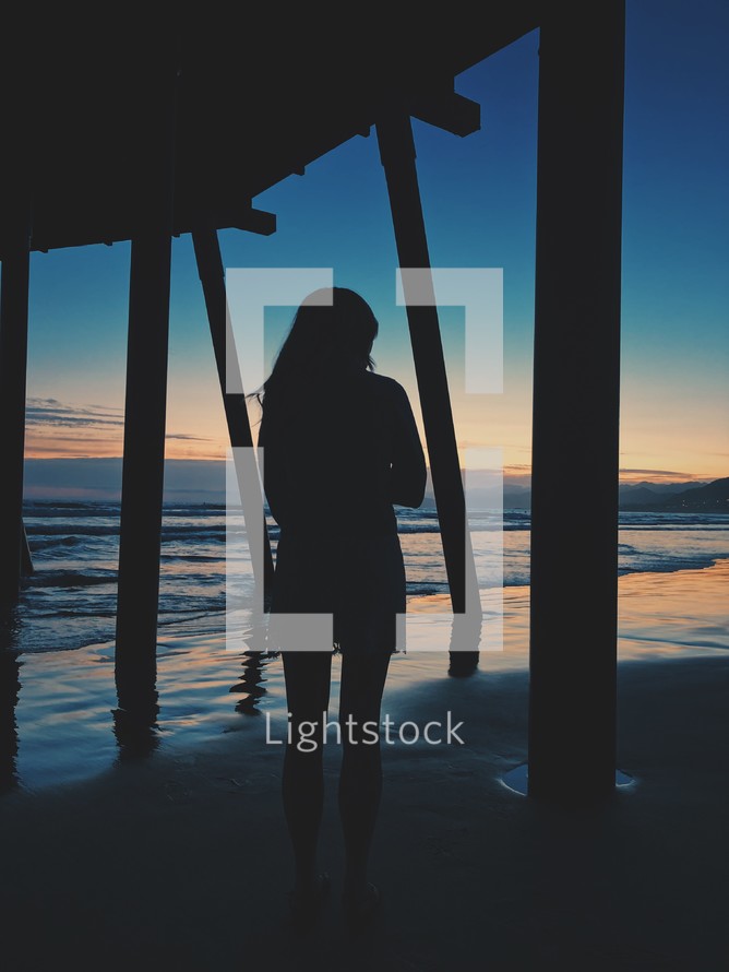 silhouette of a woman standing under a pier 