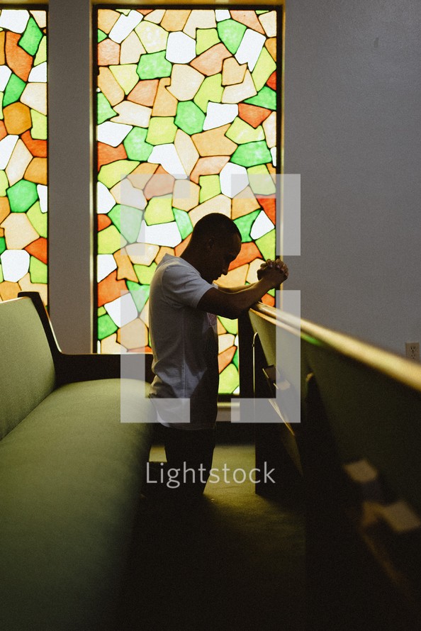 man kneeling in prayer alone in a church 
