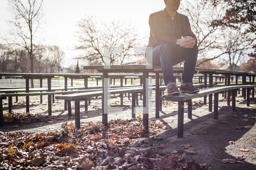 a man sitting on a picnic table in a park in fall 