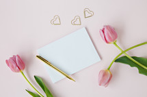 pink tulips on a light pink background with envelope and pen 