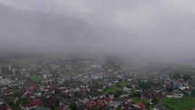 Drone captures a forward view of a quaint village nestled in the Dolomites as evening fog descends