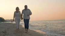 Senior couple running on the beach at sunset